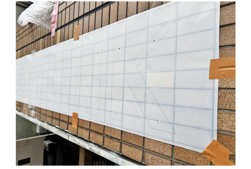 ステンレスチャンネル文字の取付の為に壁面に穴をあける風景